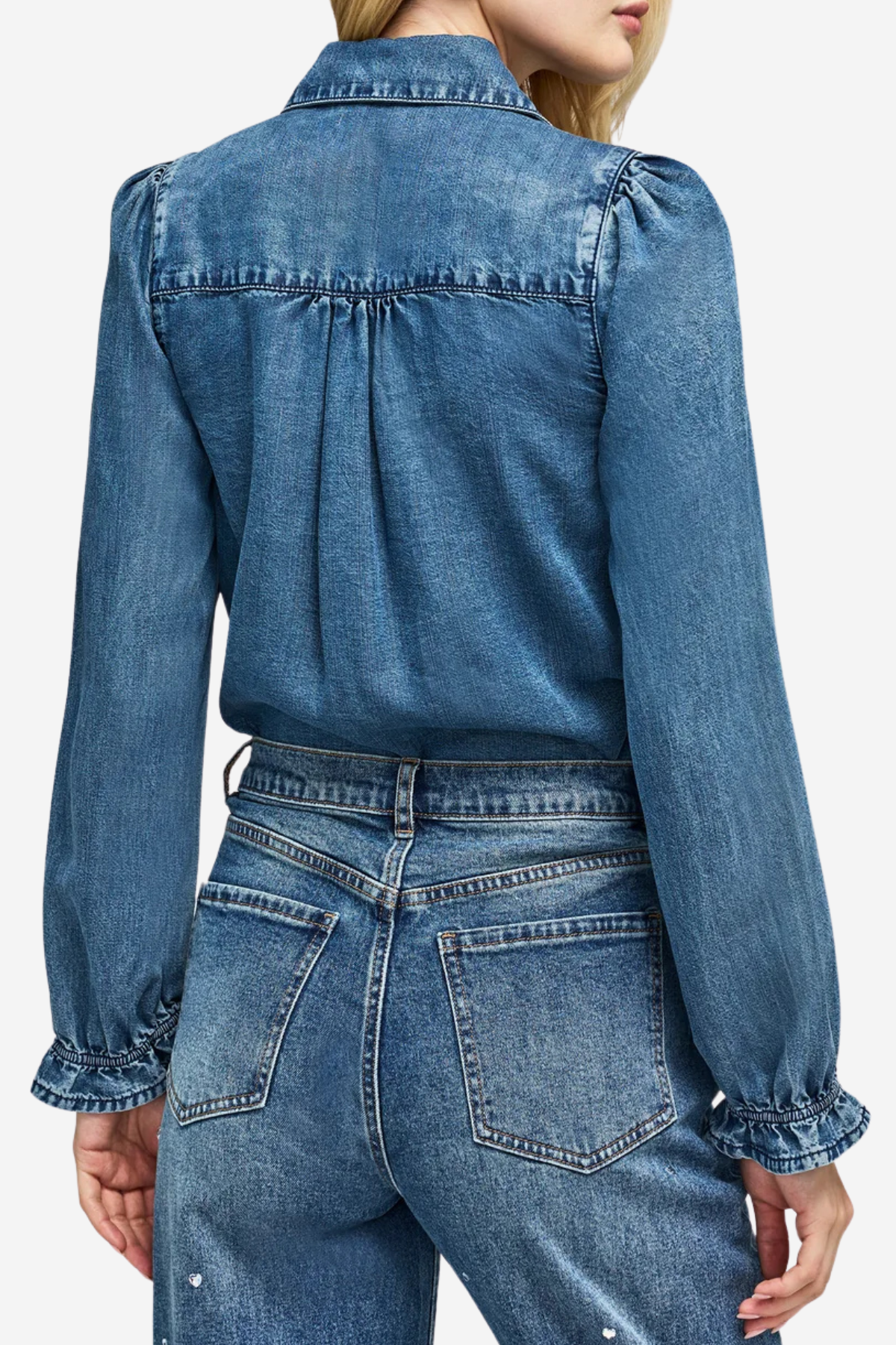 A close-up back view of a model wearing a blue denim long-sleeve blouse with gathered puff sleeves and matching blue denim jeans.