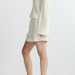 side view of woman in white sweater and shorts on white background 