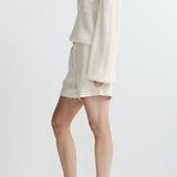 side view of woman in white sweater and shorts on white background 