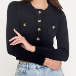 Woman wearing a black long-sleeve top with gold buttons and light blue jeans on a white background