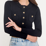 Woman wearing a black long-sleeve top with gold buttons and light blue jeans on a white background