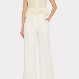 A model wearing a cream-colored short-sleeve knit top with a fringed peplum hem and matching cream wide-leg trousers, shown against a light gray studio background.