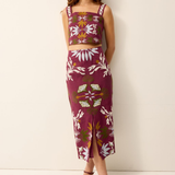 A woman modeling a matching two-piece set featuring a sleeveless crop top and a midi skirt, both in a deep magenta color with a white floral and green botanical pattern, set against a plain off-white studio background.