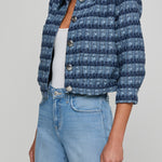 Person wearing a blue textured jacket and light blue jeans on a plain background