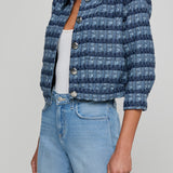 Person wearing a blue textured jacket and light blue jeans on a plain background