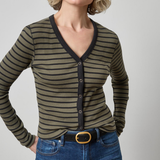 A woman wearing a ribbed long-sleeve cardigan with horizontal olive green and black stripes, paired with blue jeans and a black belt, against a plain light gray studio background.