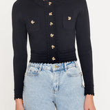 Black cardigan with gold buttons worn by a person, paired with light blue jeans on a white background