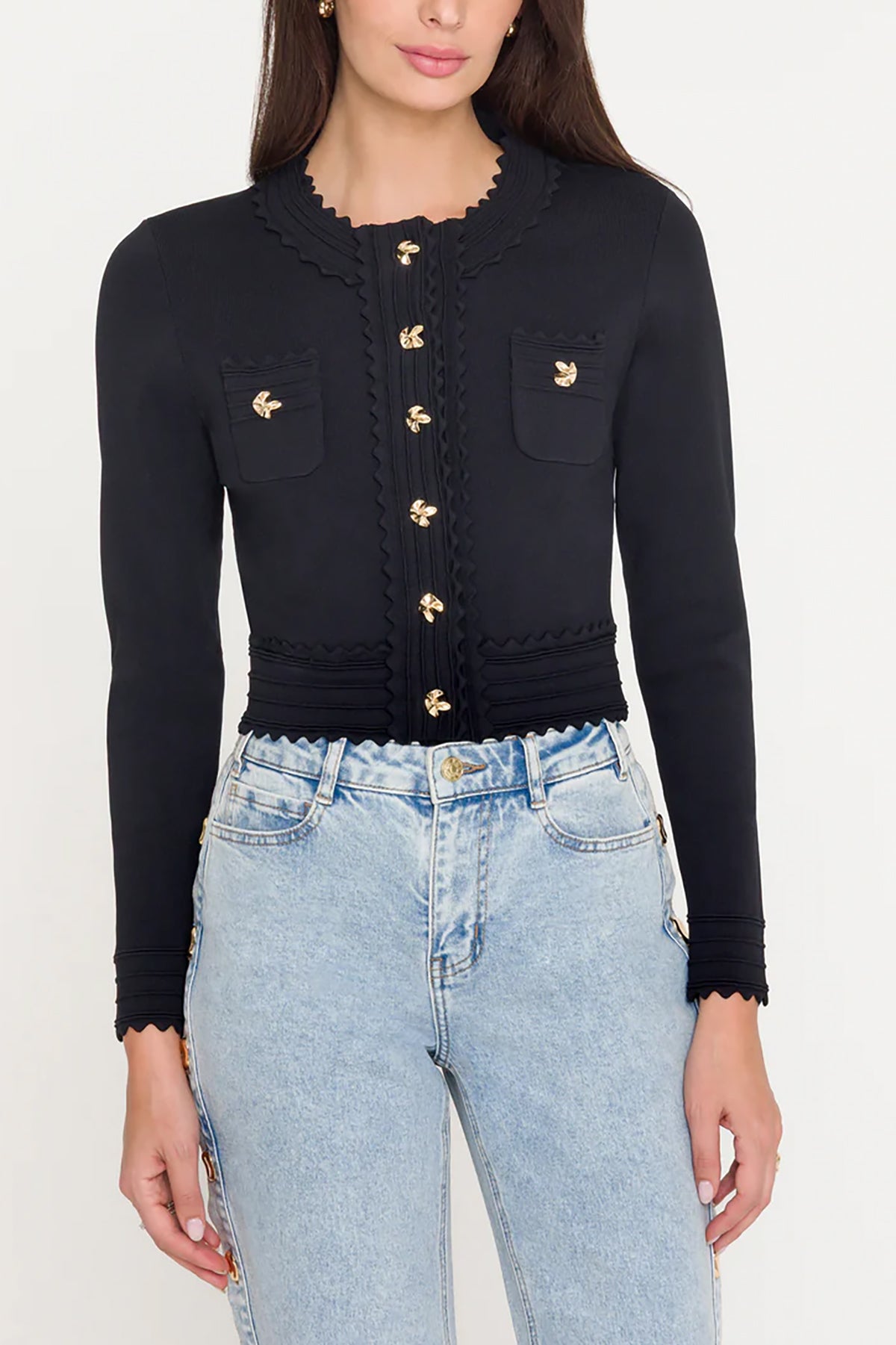 Black cardigan with gold buttons worn by a person, paired with light blue jeans on a white background