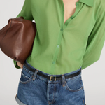 Person wearing a green shirt and denim shorts holding a brown bag on a white background