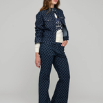 A woman modeling a matching navy blue patterned jacket and wide-leg trousers set, styled with a white top, against a neutral gray studio background.