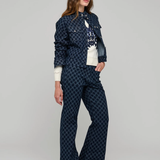 A woman modeling a matching navy blue patterned jacket and wide-leg trousers set, styled with a white top, against a neutral gray studio background.