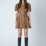 A woman modeling a brown mini shirt dress with puff sleeves, a button front, and a matching belt with a silver buckle, paired with black knee-high boots against a light gray studio background.