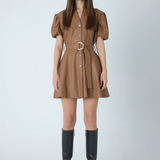 A woman modeling a brown mini shirt dress with puff sleeves, a button front, and a matching belt with a silver buckle, paired with black knee-high boots against a light gray studio background.