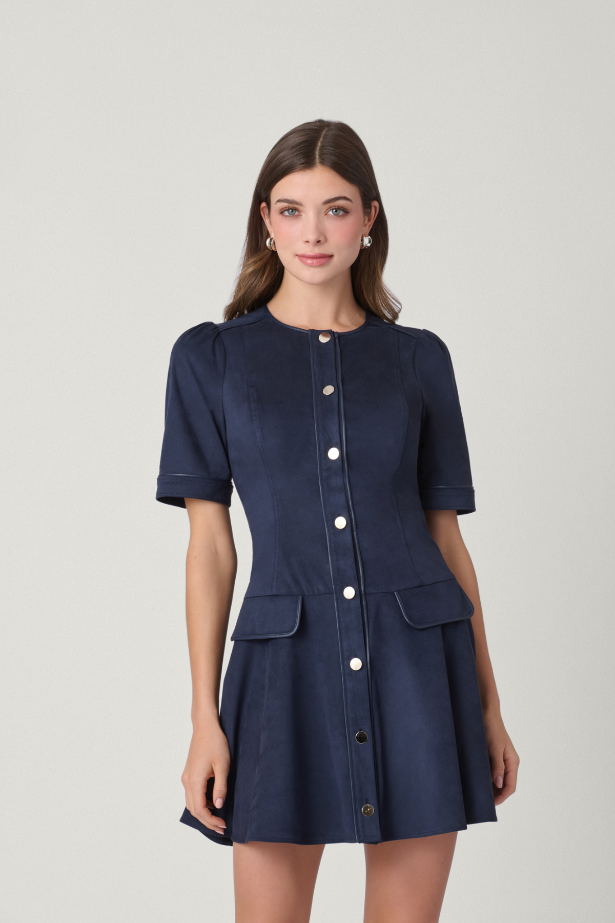 Woman wearing a navy blue dress with buttons on a light gray background