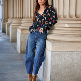 Woman leaning against a stone column wearing a patterned sweater and jeans.