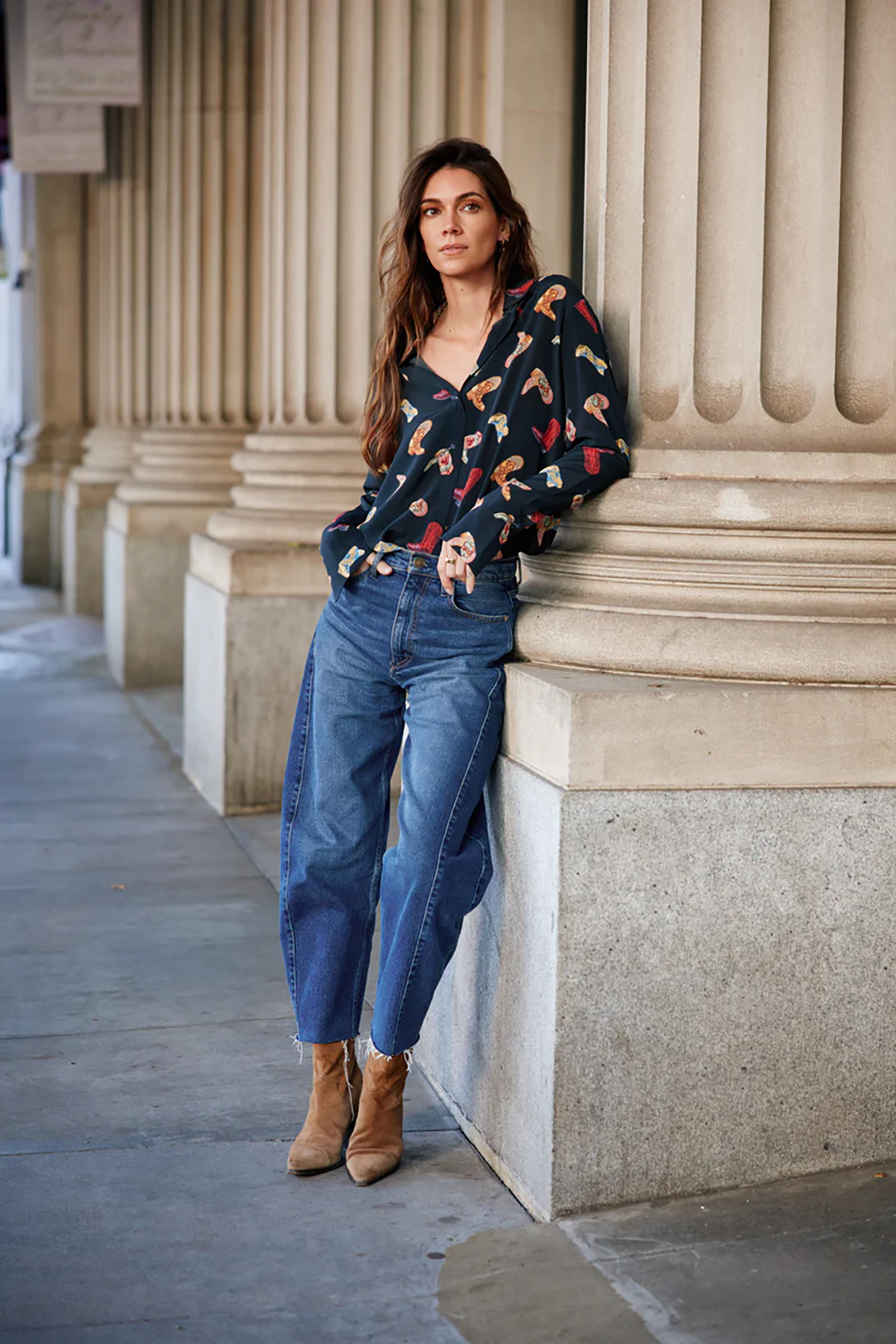 Woman leaning against a stone column wearing a patterned sweater and jeans.
