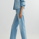 Person wearing a light blue denim jacket and jeans on a plain background