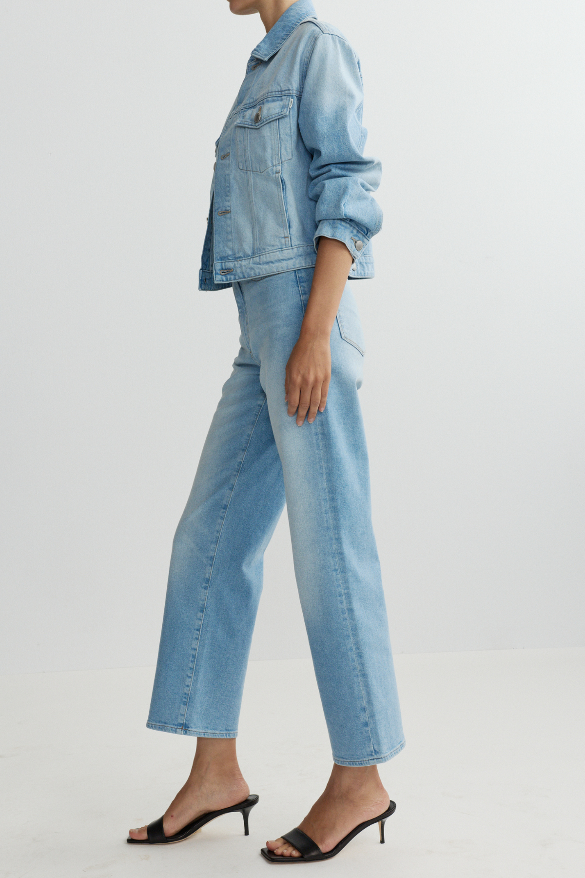 Person wearing a light blue denim jacket and jeans on a plain background