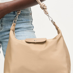 Beige handbag held by a person wearing blue jeans on a white background