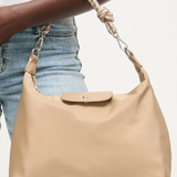 Beige handbag held by a person wearing blue jeans on a white background