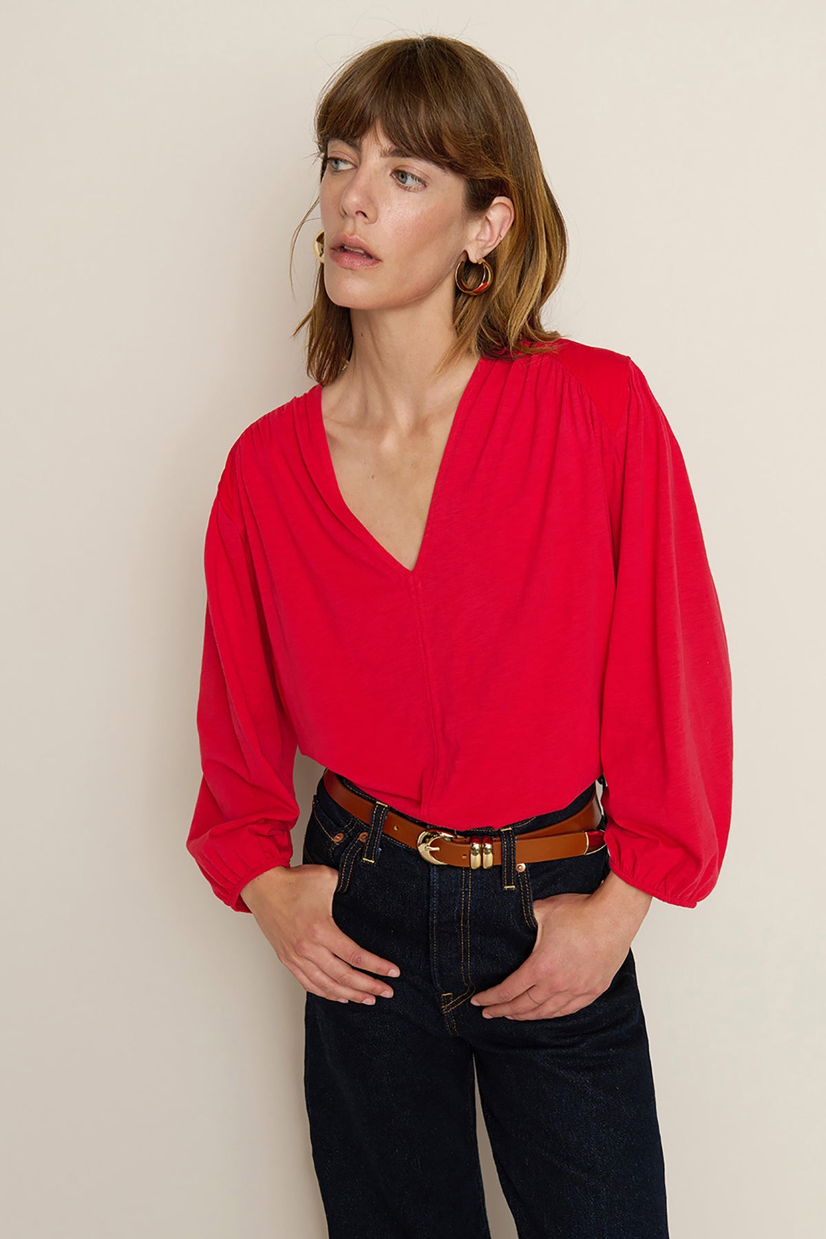 Woman wearing a red blouse and black pants against a beige background