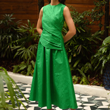 Woman in a green dress standing on a patterned floor with plants in the background