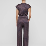 A model viewed from the back wearing a matching short-sleeve top and wide-leg trousers set in a dark purple and black geometric pattern, set against a plain light gray background.