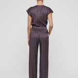 A model viewed from the back wearing a matching short-sleeve top and wide-leg trousers set in a dark purple and black geometric pattern, set against a plain light gray background.