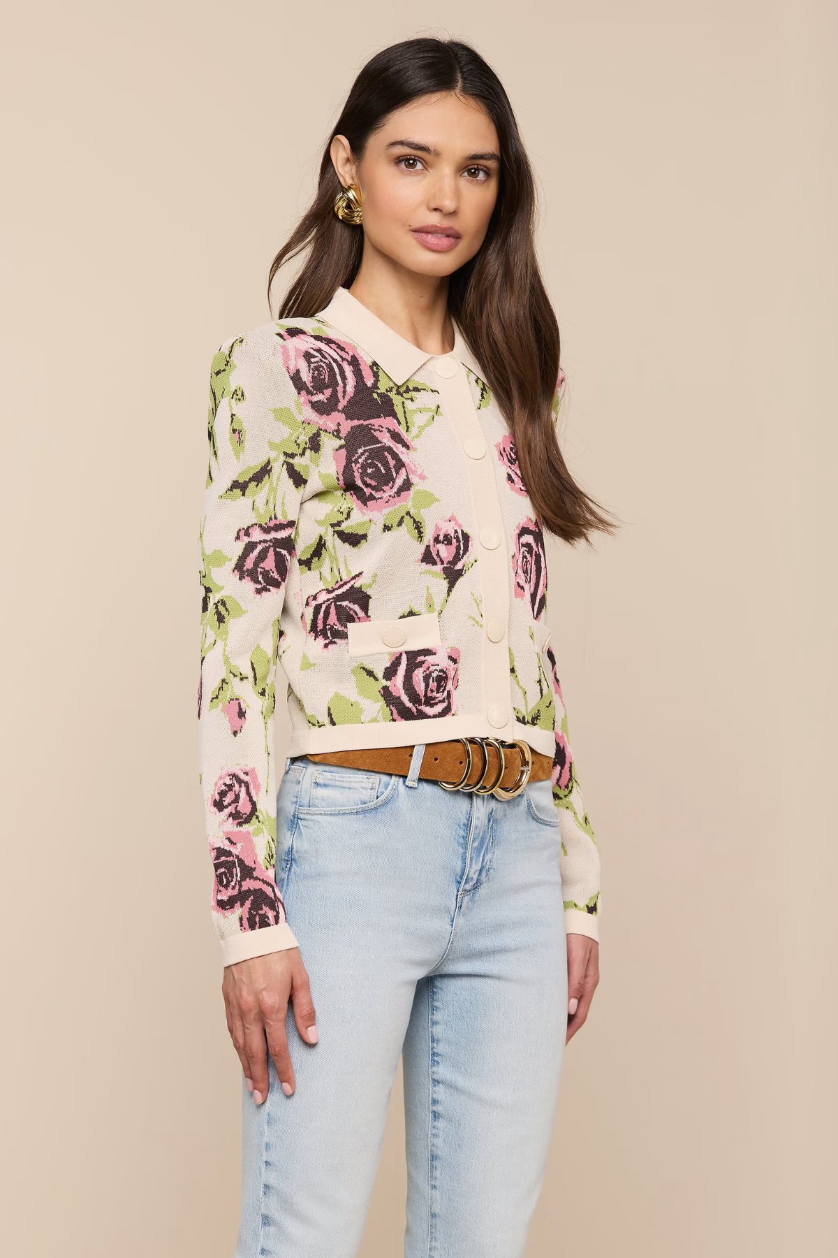 Woman wearing a floral sweater and light blue jeans against a beige background