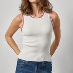 Woman wearing a white ribbed tank top with red and orange trim and blue jeans on a light gray background