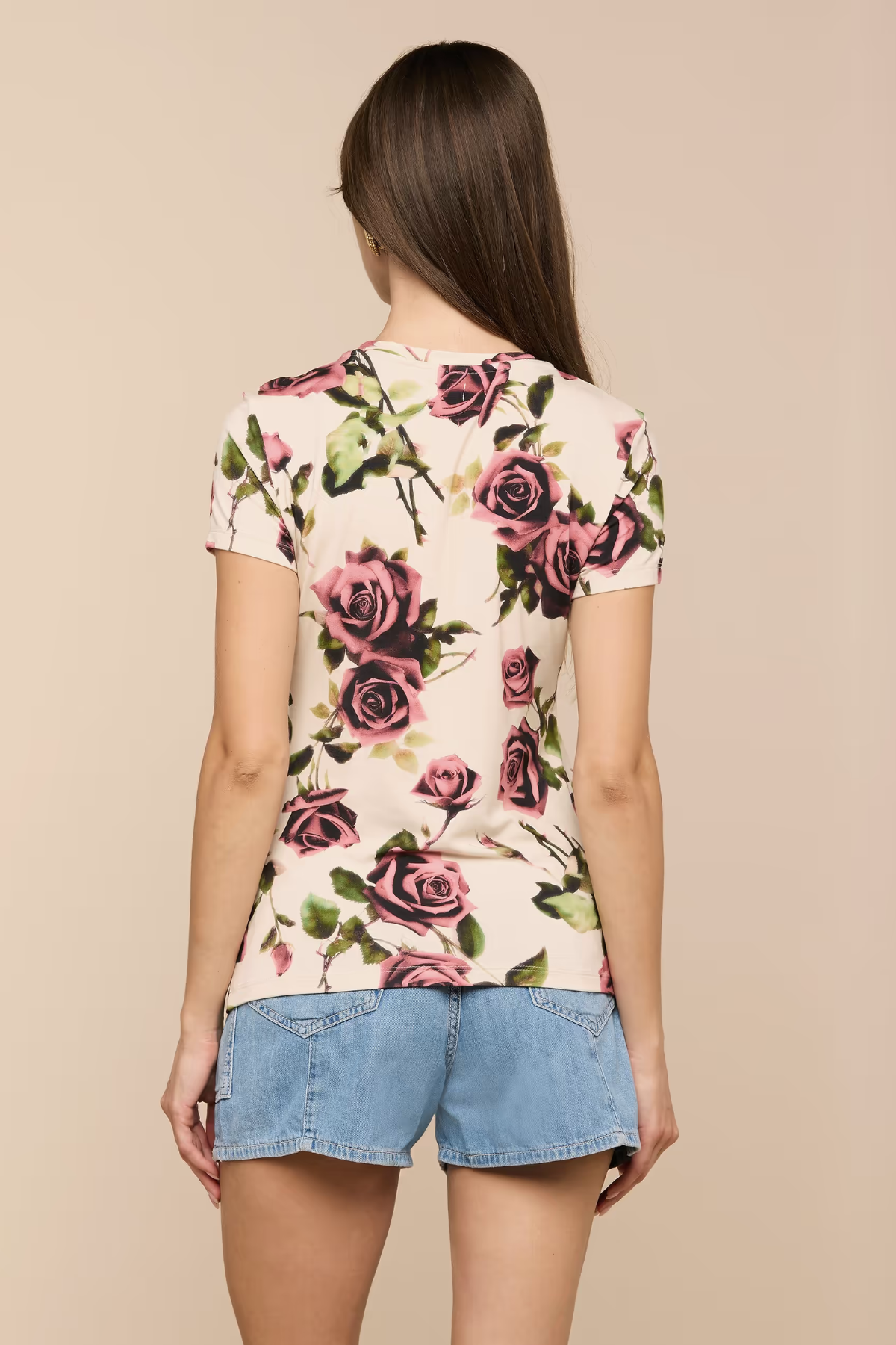 Woman wearing a floral top and denim shorts on a beige background
