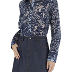A woman wearing a long-sleeve button-up shirt with a navy and beige abstract botanical pattern, tucked into a dark blue denim mini skirt, against a plain white background.