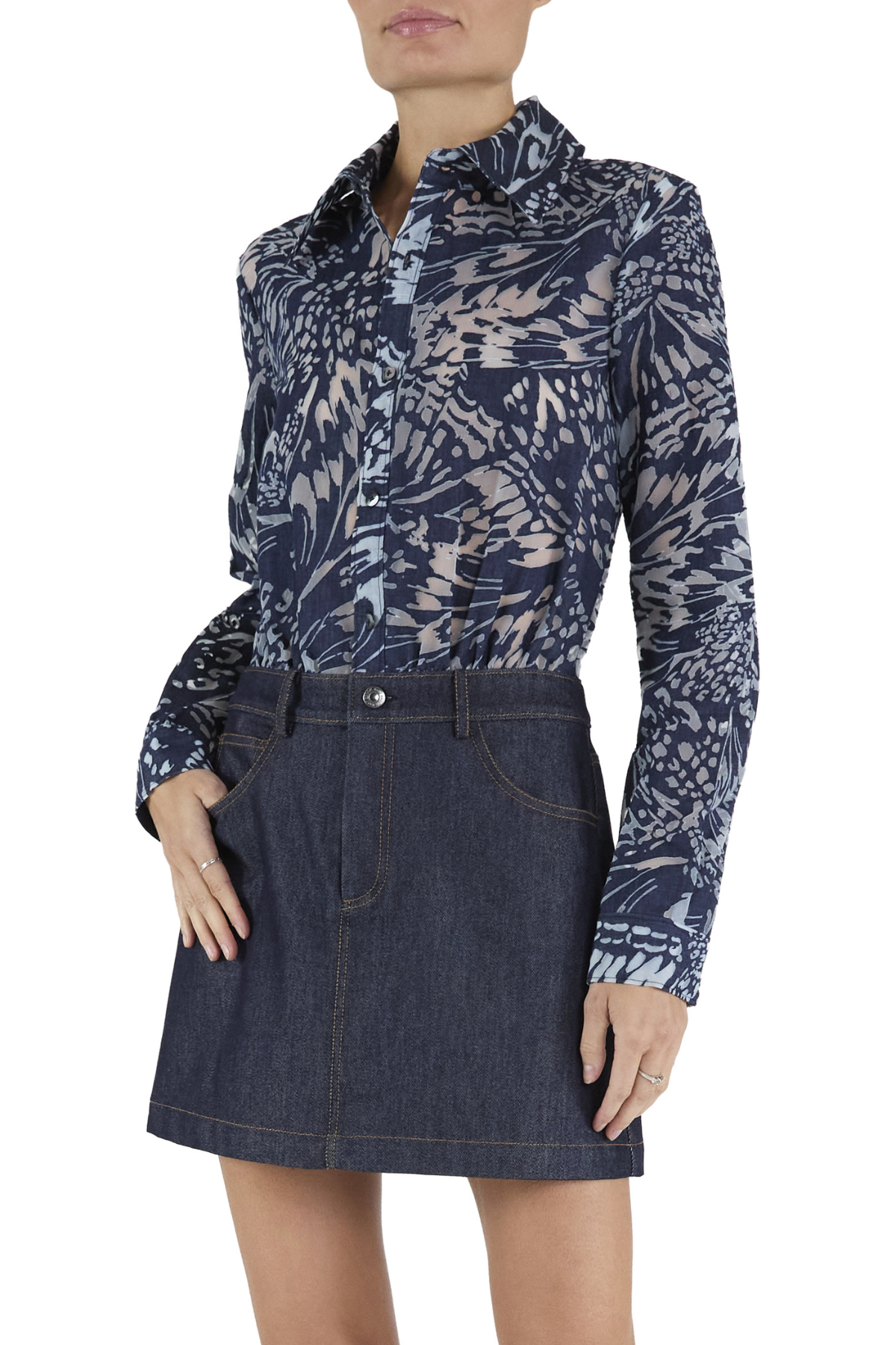 A woman wearing a long-sleeve button-up shirt with a navy and beige abstract botanical pattern, tucked into a dark blue denim mini skirt, against a plain white background.