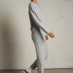 Woman wearing a light grey long-sleeve knit top with a relaxed fit, photographed against a soft neutral backdrop.