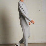 Woman wearing a light grey long-sleeve knit top with a relaxed fit, photographed against a soft neutral backdrop.