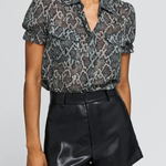 A model wearing a short-sleeve button-up blouse with a gray and black snakeskin pattern, paired with black faux-leather shorts, against a light gray studio background.