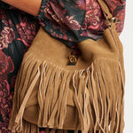 Tan suede handbag with fringe details worn by a person in a floral dress.