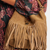 Tan suede handbag with fringe details worn by a person in a floral dress.
