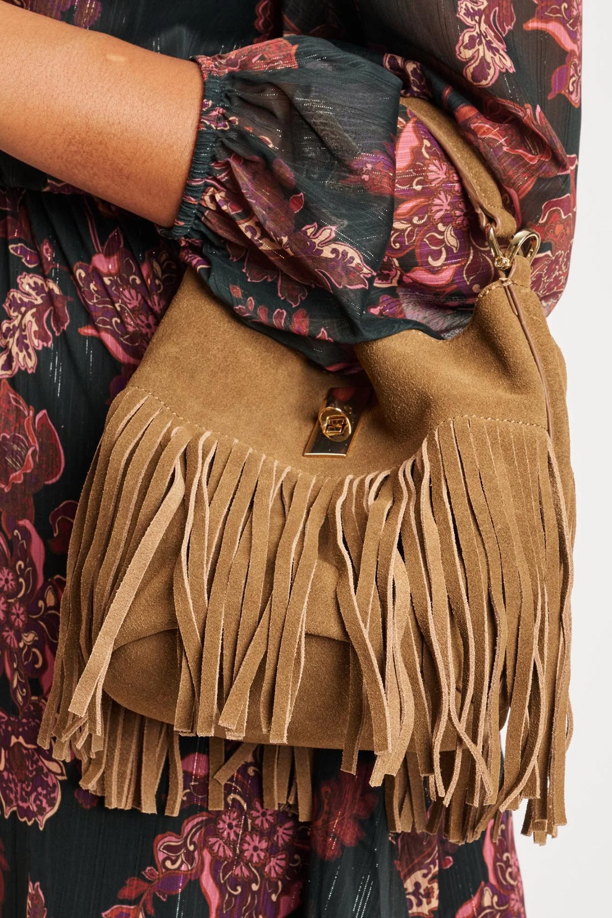 Tan suede handbag with fringe details worn by a person in a floral dress.