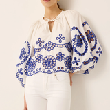 Woman wearing a white blouse with blue floral embroidery against a plain background