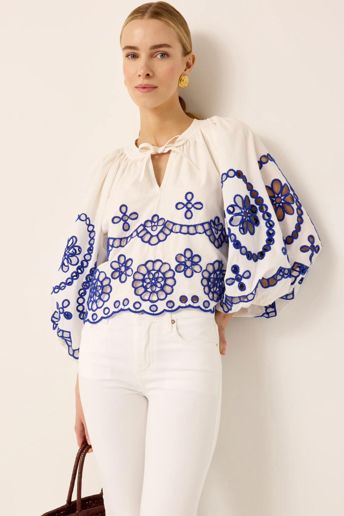 Woman wearing a white blouse with blue floral embroidery against a plain background
