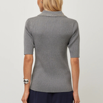 A woman viewed from the back wearing a gray short-sleeve ribbed knit top with a decorative silver beaded collar, paired with navy pants, against a light gray studio background.