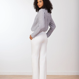 Woman wearing a gray sweater and white pants standing against a plain white background