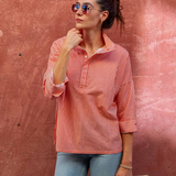 woman in striped collared button down standing by brick wall outside 