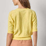 Woman wearing a yellow top and pink pants against a plain background