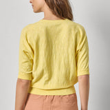 Woman wearing a yellow top and pink pants against a plain background