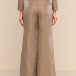 A model shown from the back wearing a matching taupe-beige two-piece set with wide-leg trousers and a cropped long-sleeve top, both featuring gold button accents on the cuffs.