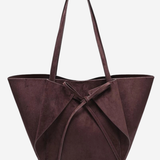 A dark plum purple suede tote bag with a large bow detail at the front and two shoulder straps, shown against a plain light gray background.