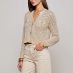 Woman wearing a beige knitted cardigan and light-colored pants against a plain background