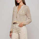 Woman wearing a beige knitted cardigan and light-colored pants against a plain background